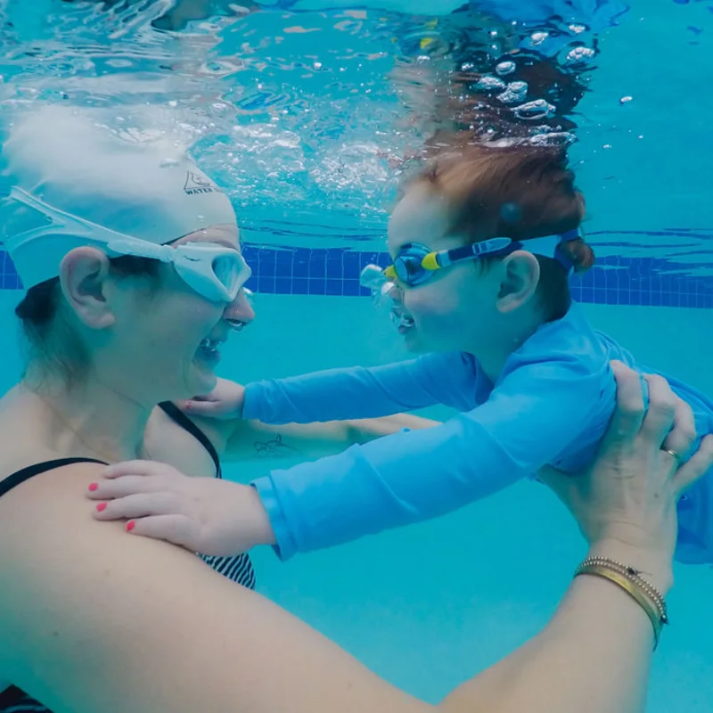 Instructor and young swimmer underwater, smiling together
